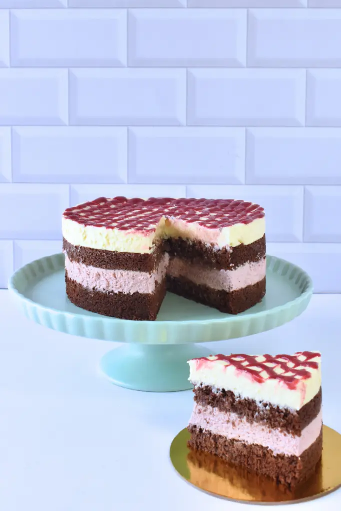 Torta Primavera de Mora de Pepos Cake Medellín, con capas de bizcocho de chocolate, crema de mora y cobertura decorada con salsa de frutos rojos, presentada en un pedestal con una porción al lado.