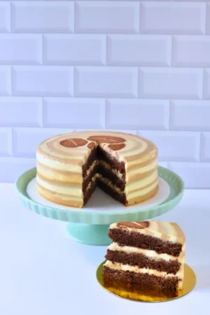 Torta de Baileys de Pepos Cake Medellín, con capas de torta de chocolate remojada en Baileys, rellena y cubierta con crema de café y crema repostera, mostrada en un pedestal con una porción al frente.